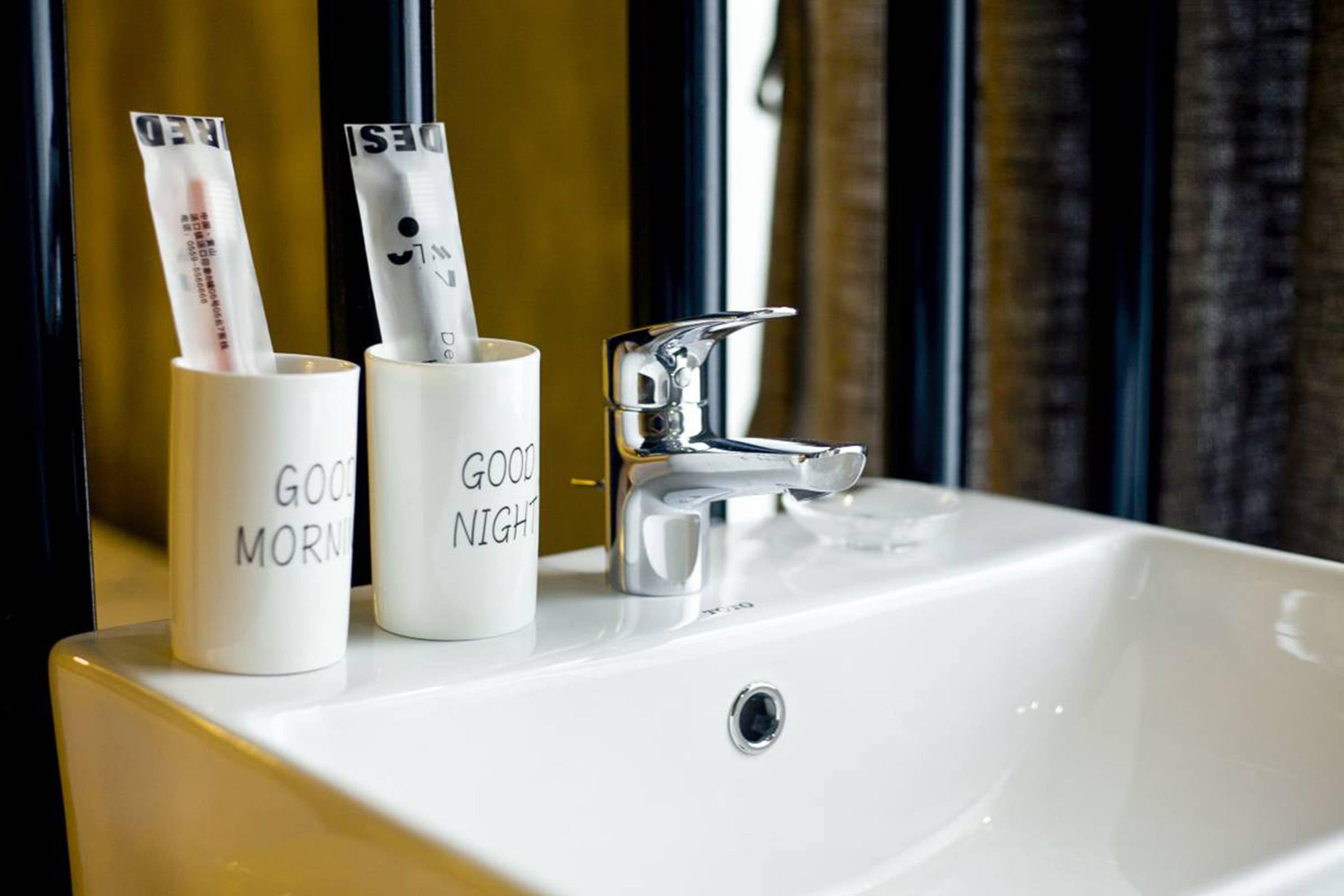 A white sink with two white mugs containing newspapers, one with "GOOD MORNING" and the other with "GOOD NIGHT".