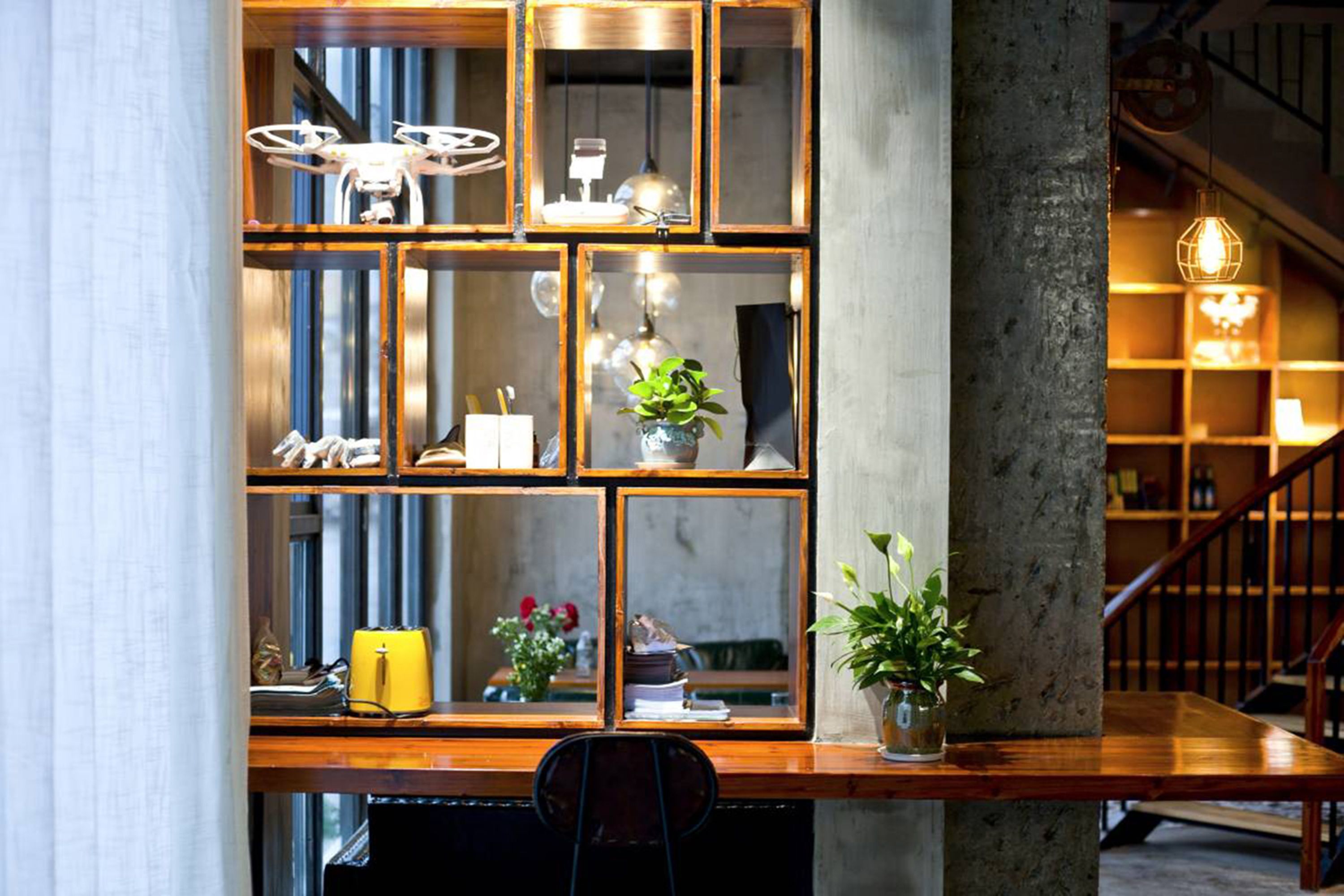 A modern interior with a wooden desk, shelves with decorative items, a potted plant, and a staircase in the background.