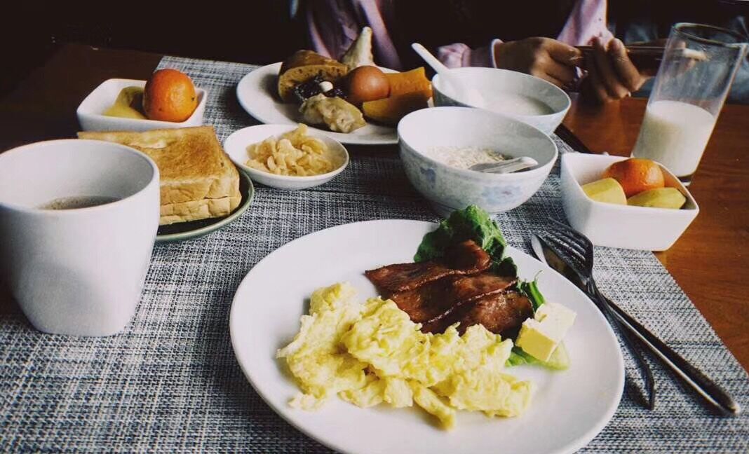 A breakfast setting with scrambled eggs, bacon, toast, and fruit on a table.