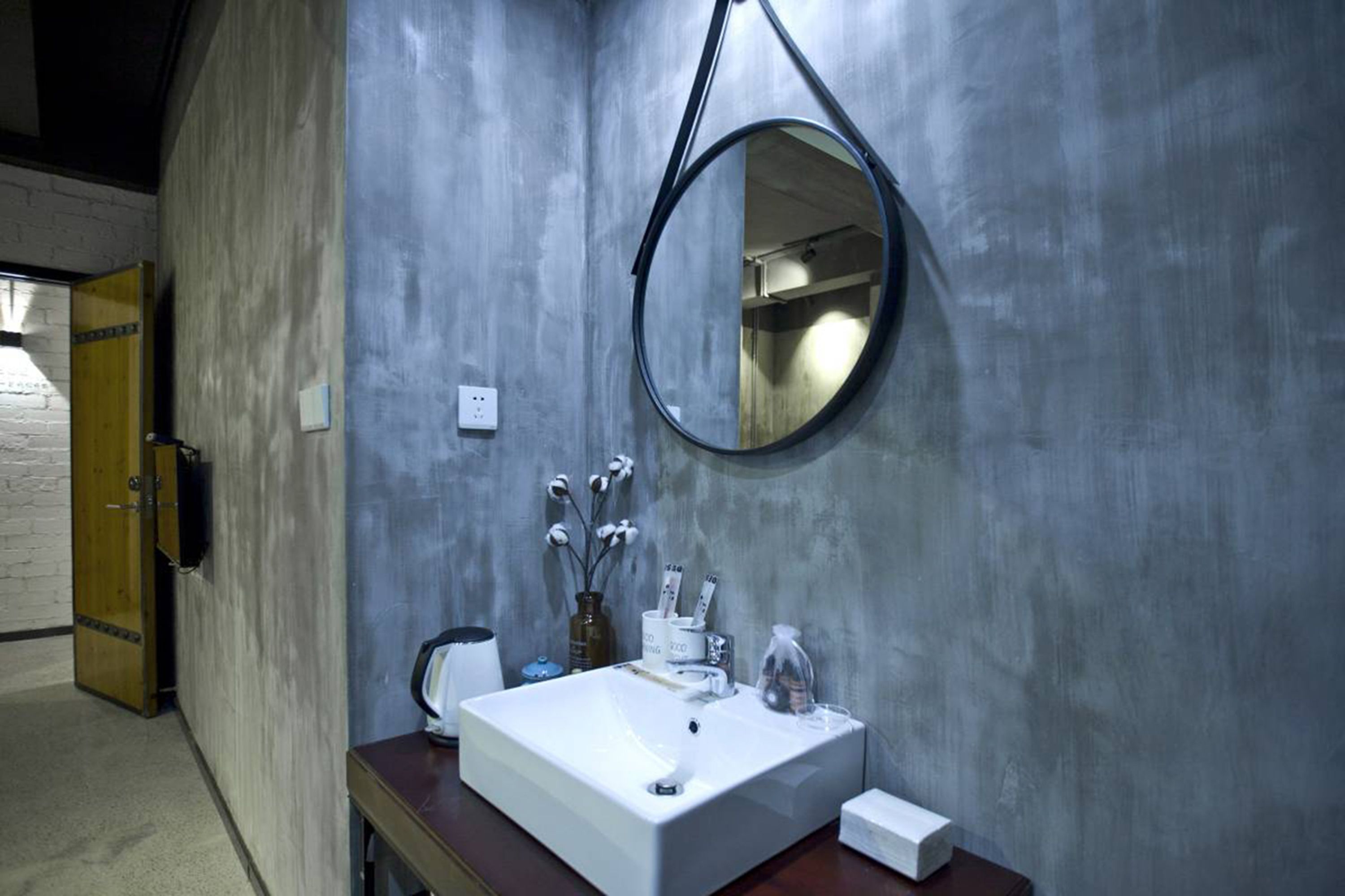 A bathroom with a rectangular sink, a round mirror, and a wooden door.