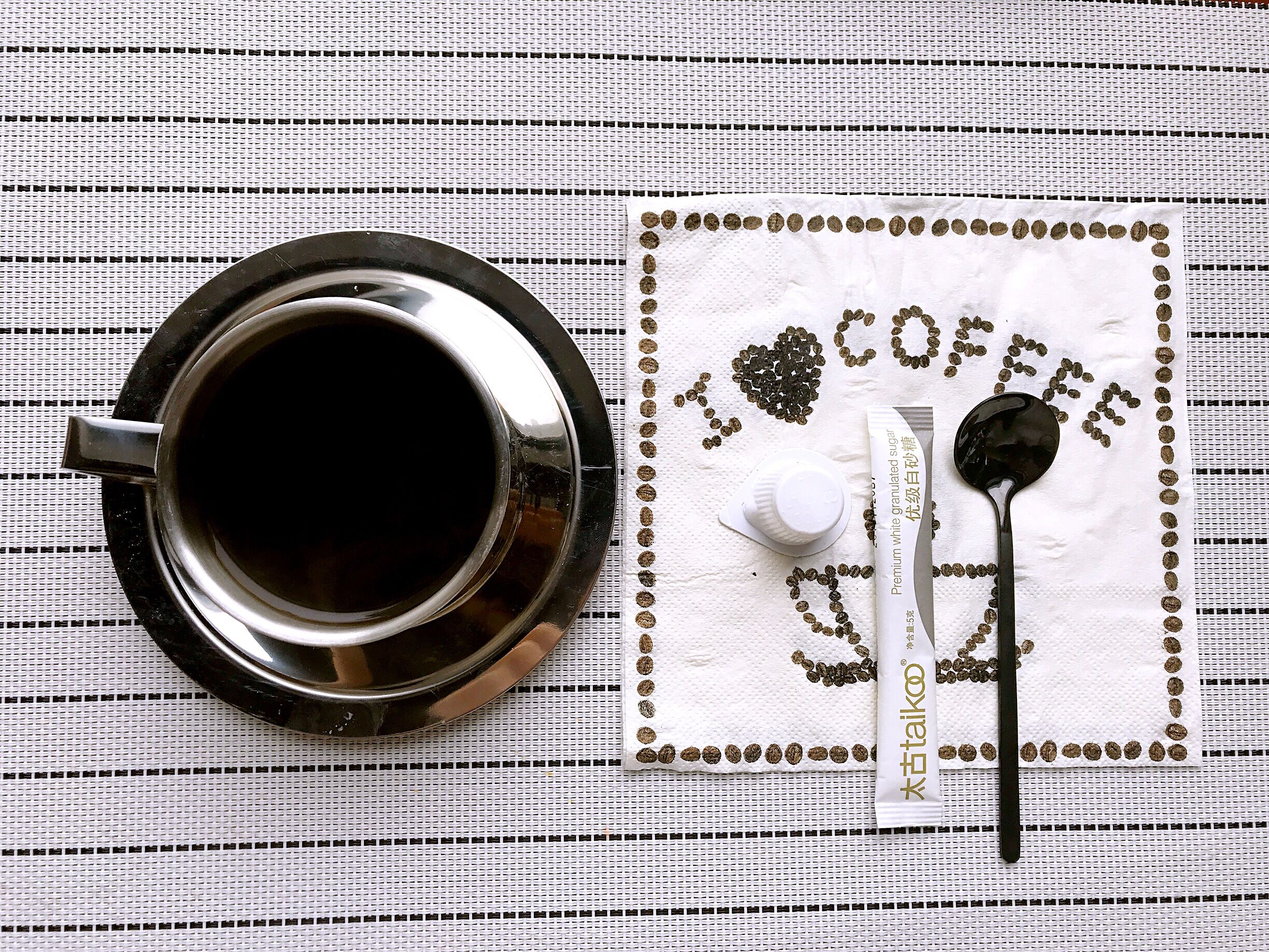 A cup of coffee on a tray with a napkin that reads "I love coffee" and a spoon.