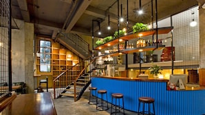 A bar area with a blue counter, wooden stools, and a staircase leading to a mezzanine with shelves of bottles and plants. - Zero Five One Seven Inn (Huangshan)