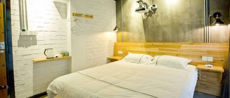 A hotel room with a large bed, wooden headboard, bedside tables, a white brick wall, and a modern light fixture.