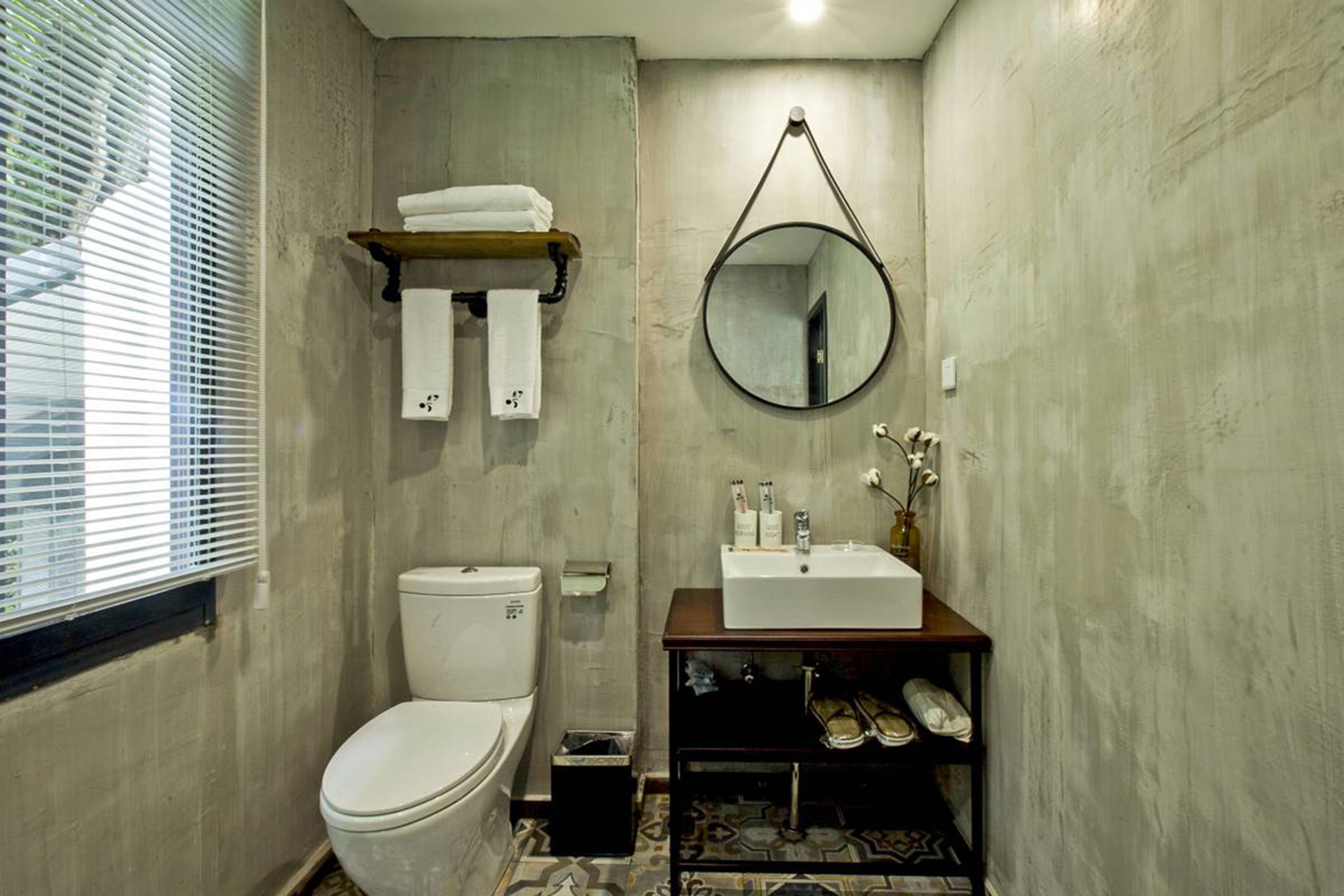 Une salle de bain comprenant des toilettes, un lavabo avec des articles de toilette, un miroir et une étagère avec des serviettes.