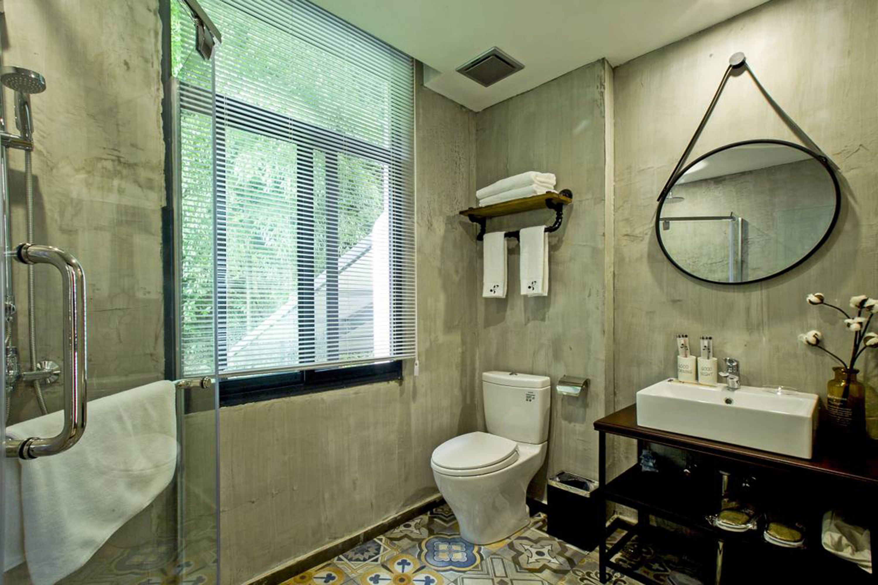 A bathroom with a shower, toilet, sink, and a window with blinds.