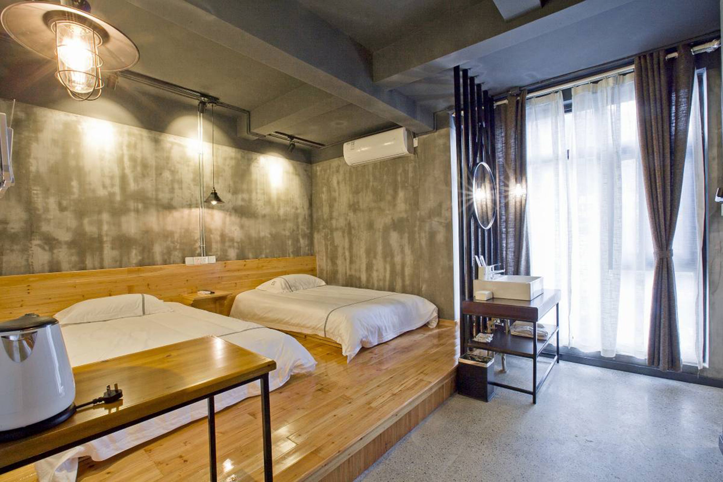 A hotel room with two beds, a wooden table, a desk with a lamp, and a window with curtains.
