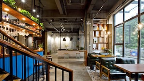 A modern bar area with wooden shelves, bar stools, and a staircase leading to a seating area with tables and chairs. - Zero Five One Seven Inn (Huangshan)