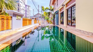 Une piscine dont le bord est revêtu de carrelage, entourée de bâtiments et d’une clôture.