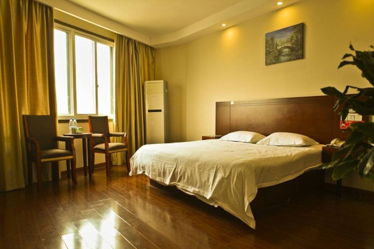 Una habitación de hotel con cama, escritorio, silla, ventana con cortinas y un cuadro en la pared.
