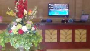 A reception desk with a television screen displaying a pool scene, a floral arrangement, and a person seated behind the desk. - GreenTree Inn Jiaxing Pinghu Zhapu Jiulong Mountain Express  Hotel (Jiaxing)