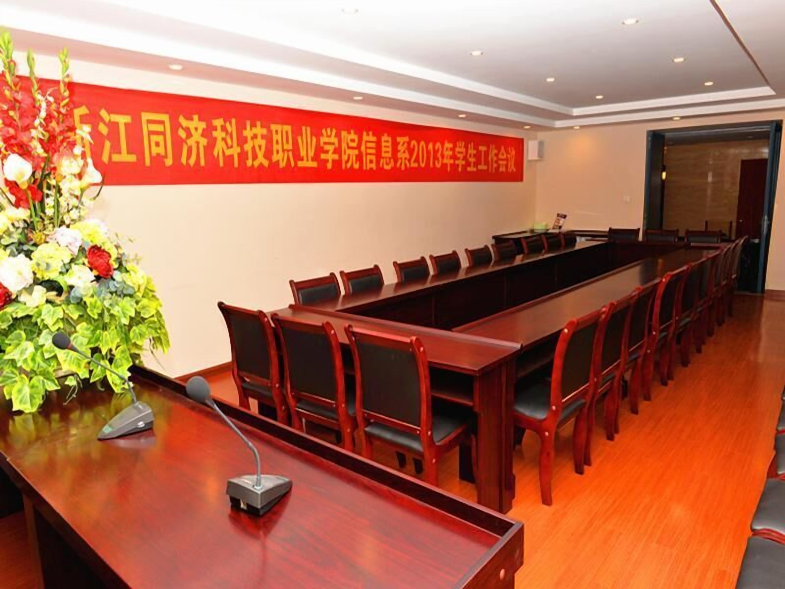 A conference room with a long table, chairs, a microphone, and a floral arrangement.