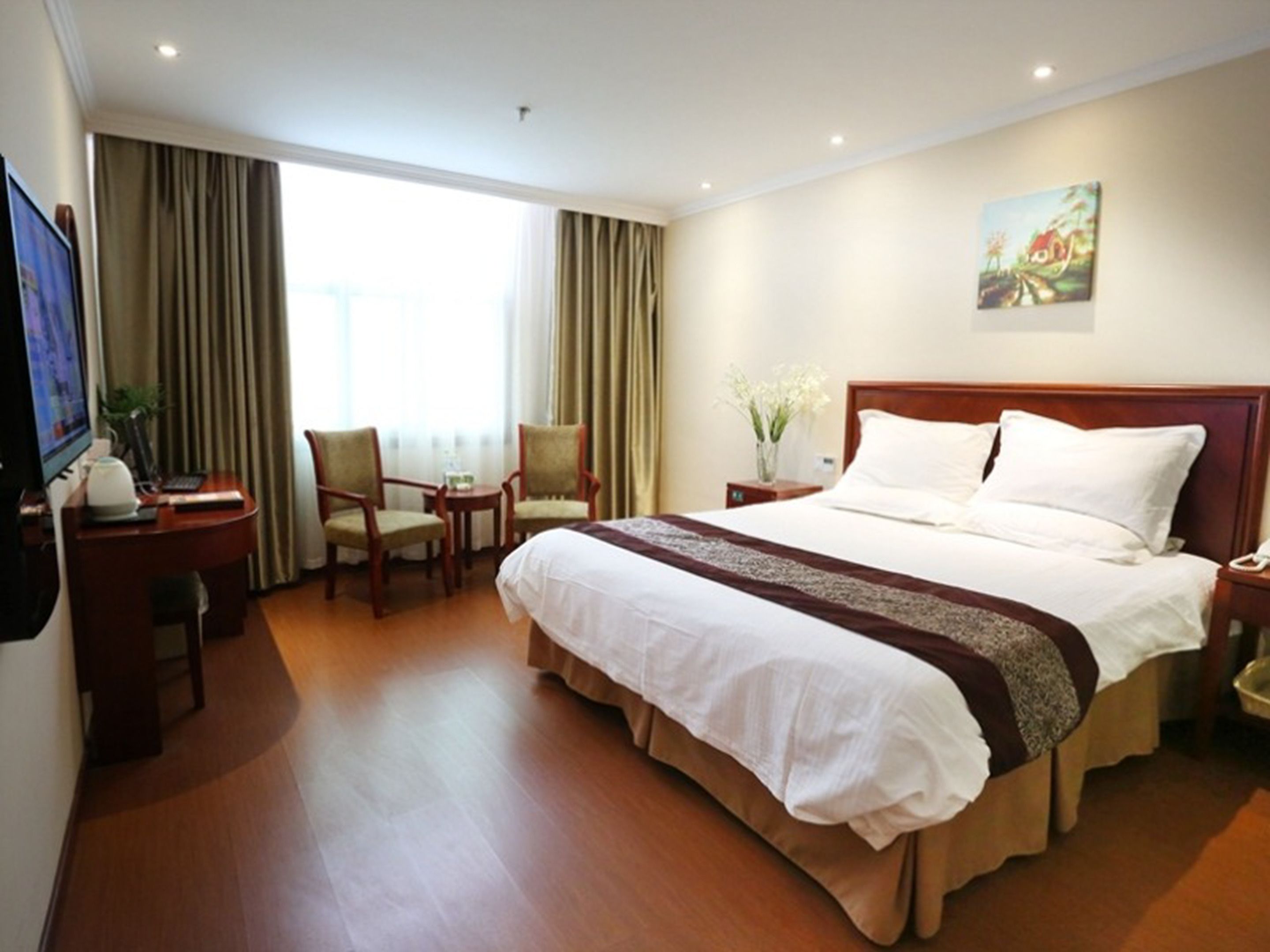 A hotel room with a large bed, a desk with a computer, two chairs, a small table, and a painting on the wall.