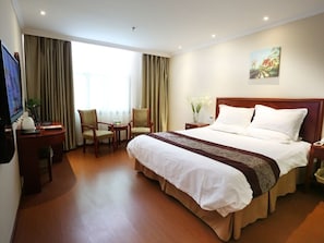 A hotel room with a large bed, a desk with a computer, two chairs, a small table, and a painting on the wall.