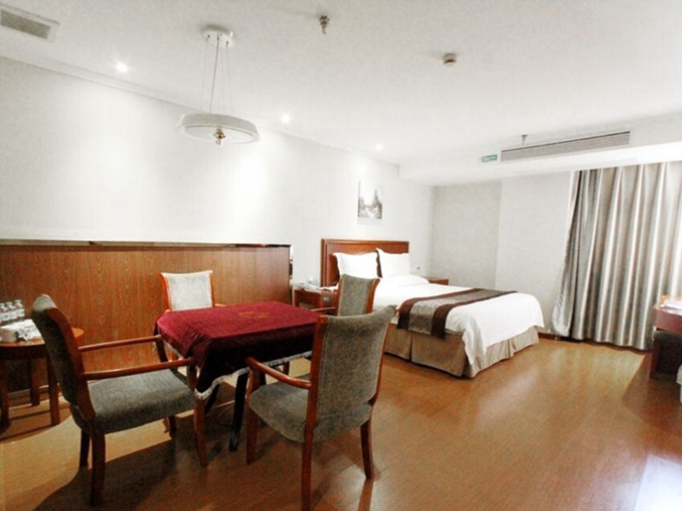 A hotel room with a wooden bed, a desk with a chair, a small table, and a red tablecloth.