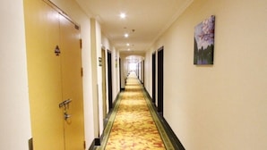 Un couloir d’hôtel avec un sol recouvert de moquette, des portes sur le côté gauche et un tableau accroché au mur de droite.