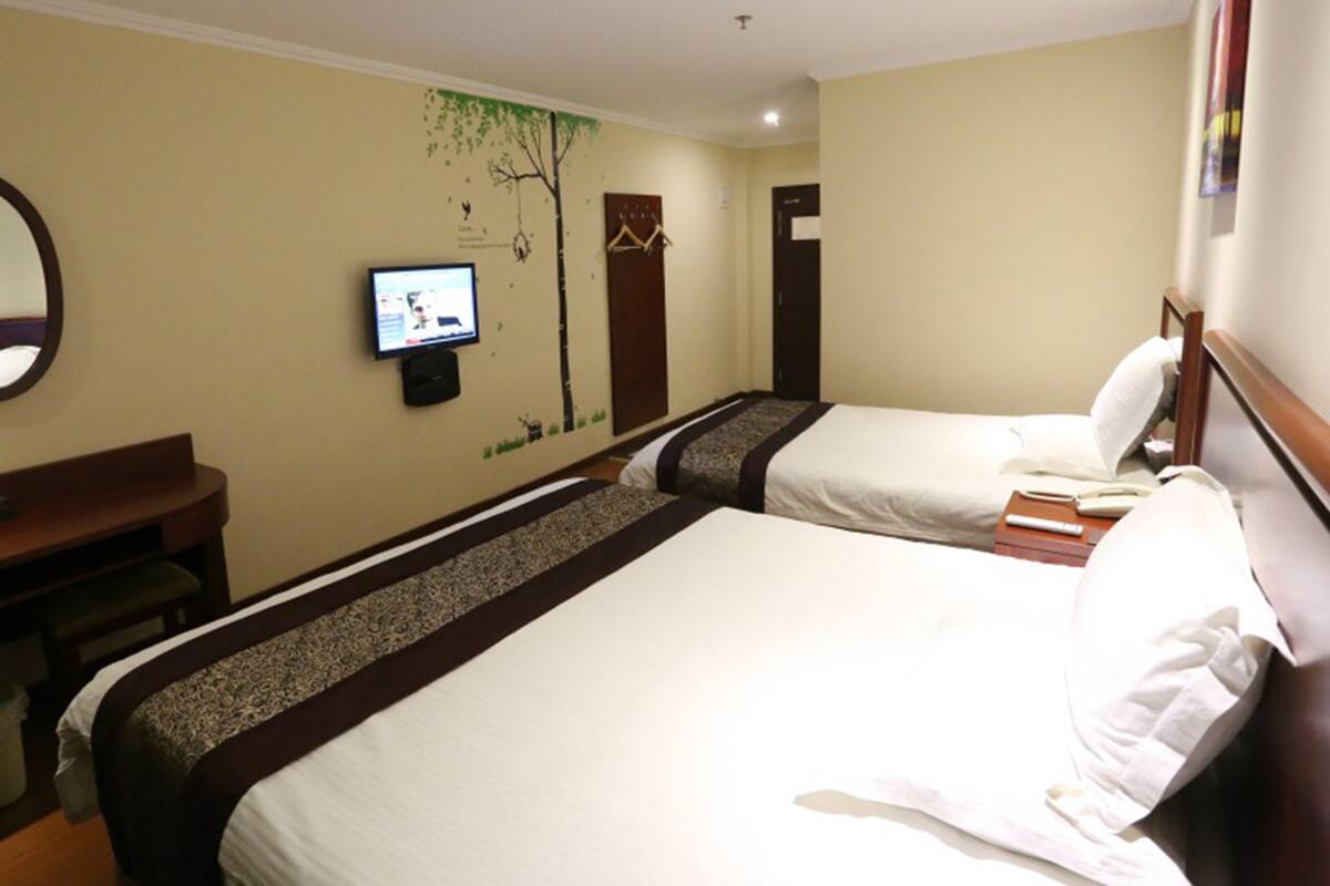 A hotel room with two beds, a desk, a television, and a door.