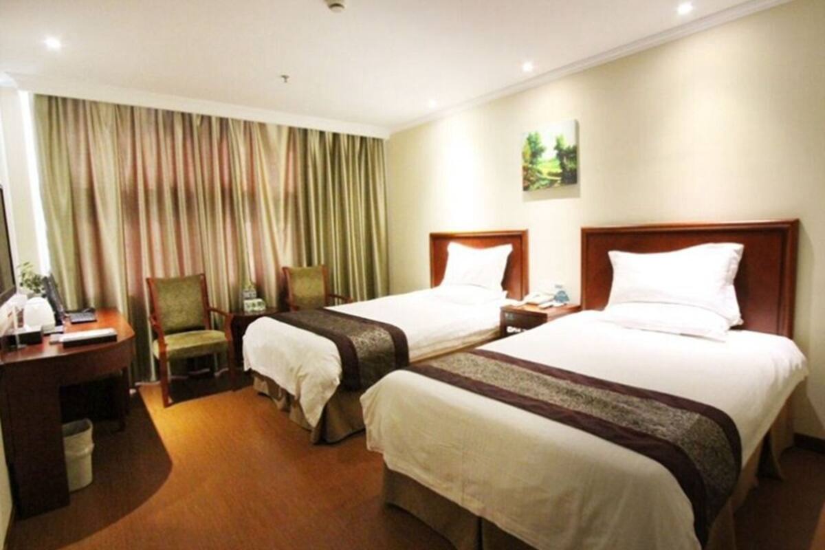 A hotel room with two beds, a desk, a chair, and a curtain.