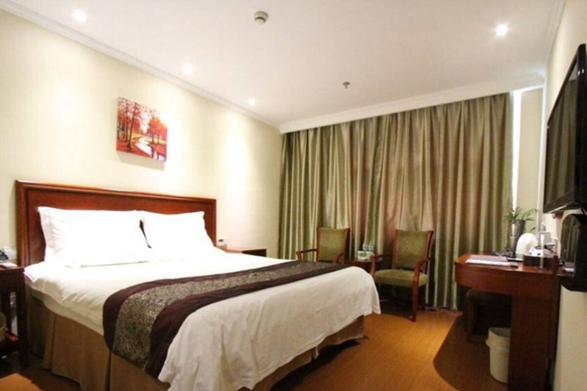 A hotel room with a large bed, a desk with a chair, a television, and a window with curtains.