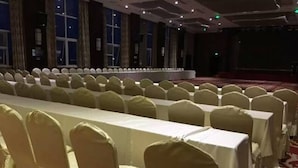 Un salón de banquetes con filas de mesas cubiertas con manteles blancos y sillas con fundas blancas.