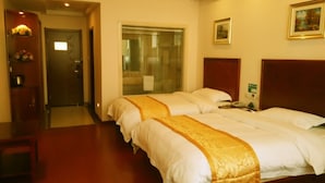 Habitación de hotel con dos camas, un cabecero de madera, una mesita de noche, un espejo y una puerta que da a un baño.