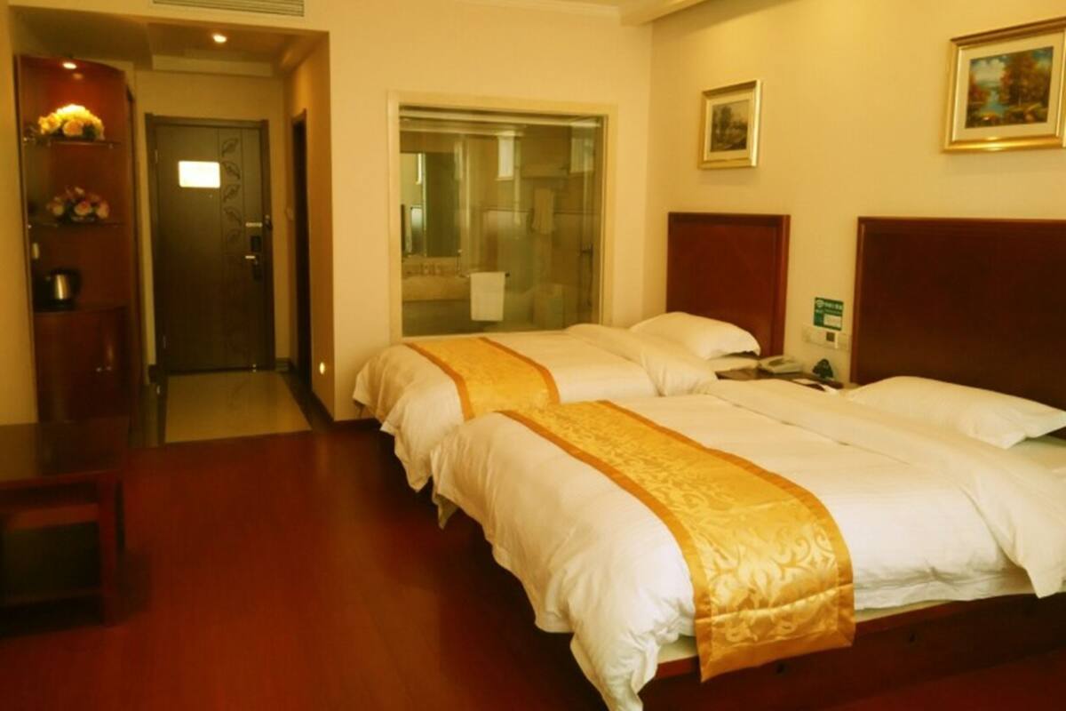 Habitación de hotel con dos camas, un cabecero de madera, una mesita de noche, un espejo y una puerta que da a un baño.