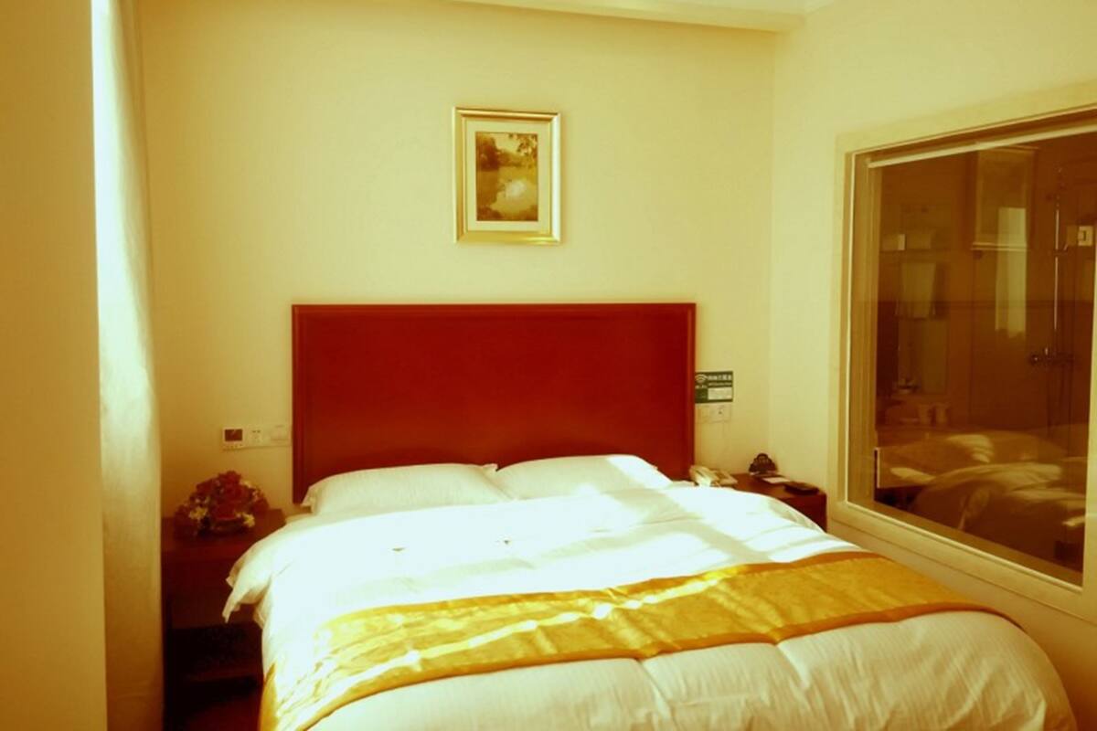 Una habitación de hotel con una cama grande, cabecera roja, un cuadro enmarcado en la pared y una ventana con vistas al exterior.
