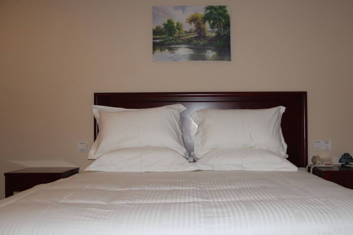 Una cama bien tendida con sábanas blancas, un cabecero de madera y un cuadro de un paisaje en la parte superior.