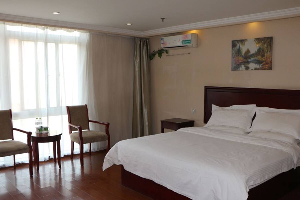 Una habitación de hotel con una cama grande, dos sillas, una mesita de noche y un cuadro en la pared.