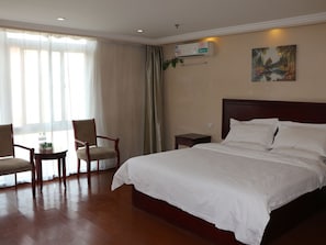 A hotel room with a large bed, two chairs, a nightstand, and a painting on the wall.