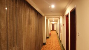 Un couloir d'hôtel avec un sol recouvert de moquette, un lambris en bois d'un côté et des portes de l'autre.