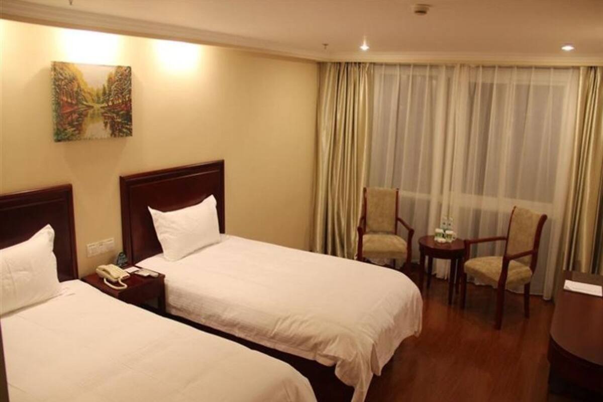Habitación de hotel con dos camas individuales, un escritorio con silla, una mesita con otra silla y un cuadro en la pared.