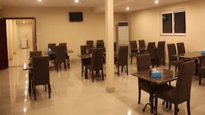 Une salle de conférence équipée de plusieurs tables et chaises, d’un téléviseur à écran plat fixé au mur et d’une fenêtre avec des stores.