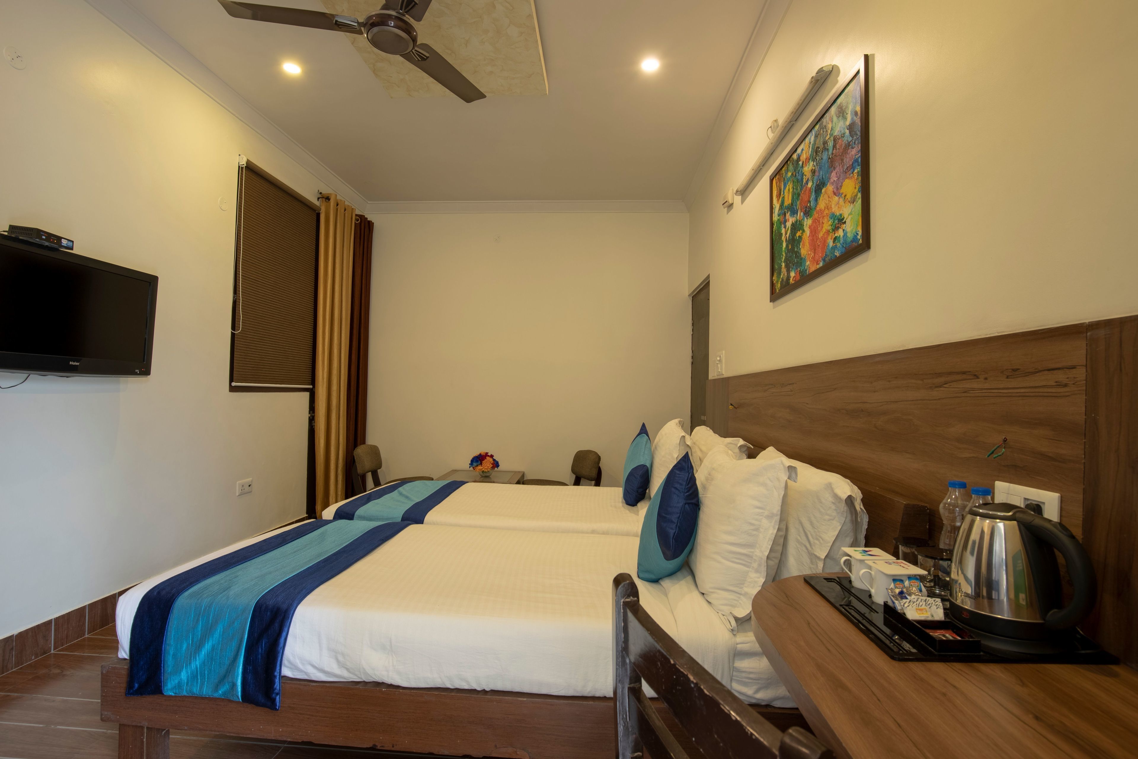 Une chambre d’hôtel avec deux lits, un ventilateur de plafond, un téléviseur à écran plat, un tableau et une machine à café sur la table de chevet.