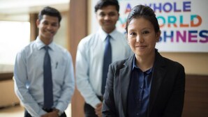Three individuals in business attire standing in a hallway with a sign that reads "WELCOME TO THE WHOLE WORLD". - Eclat Suites Mint Gomti Nagar (Lucknow)
