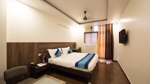 A hotel room with a bed, a desk, a chair, a TV, and a ceiling fan. - Eclat Suites Mint Gomti Nagar (Lucknow)