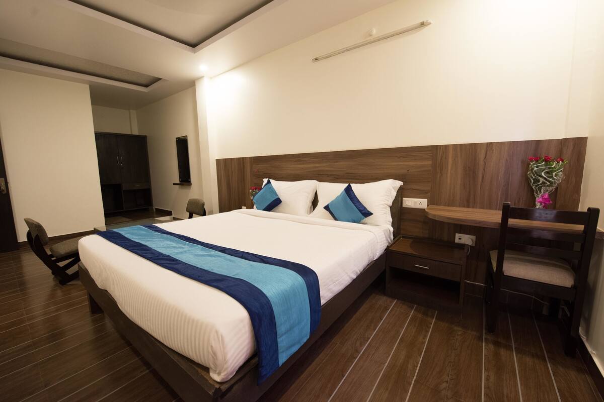 A modern hotel room with a large bed, a wooden headboard, a desk, and a chair.