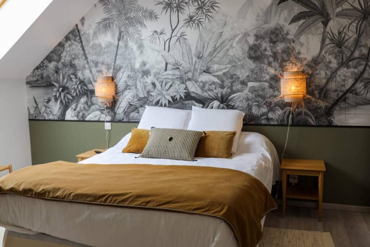 Ein Schlafzimmer mit einem großen Bett, zwei Nachttischen, einem Beistelltisch und einer Wandmalerei von tropischen Pflanzen.