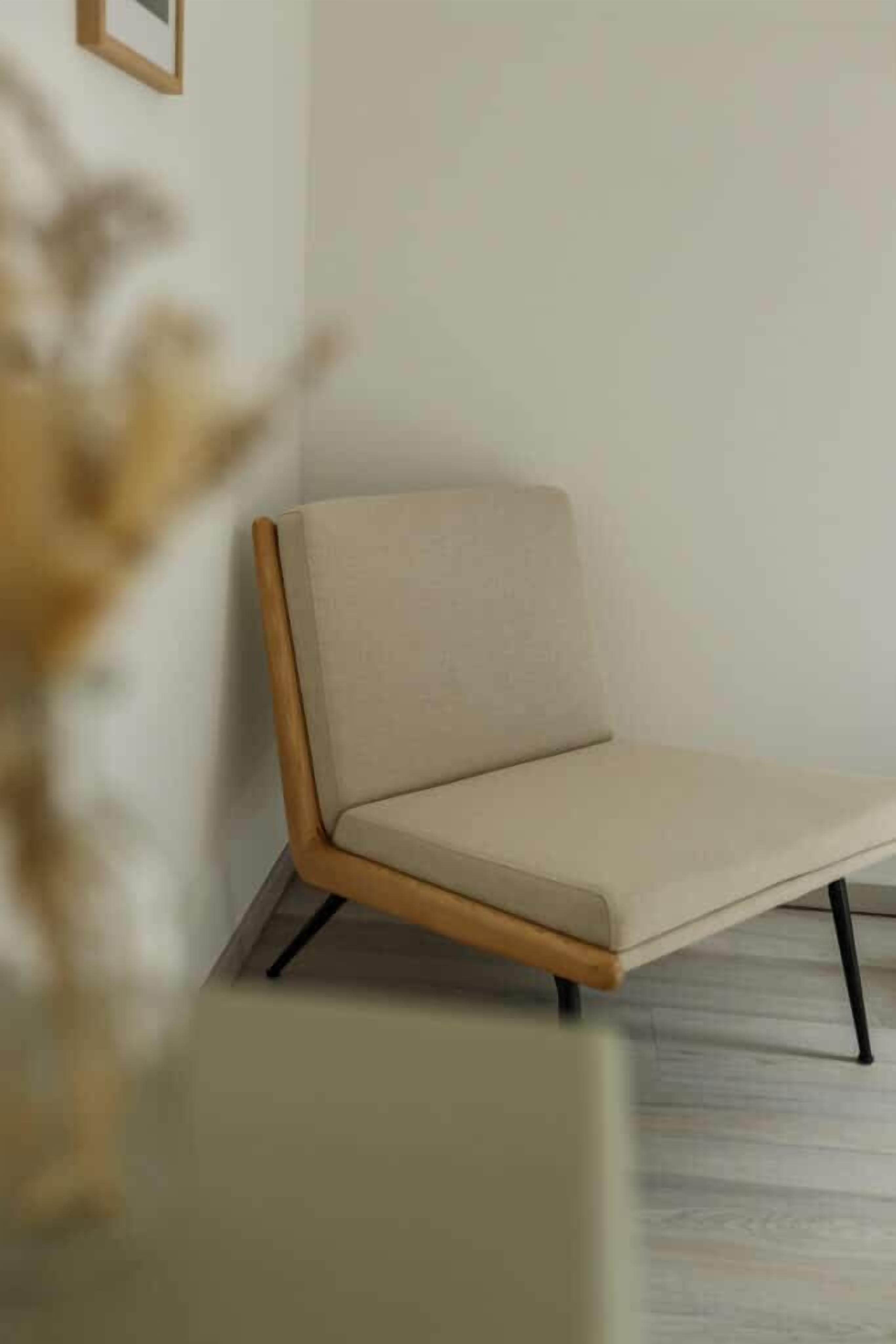 A modern chair with a wooden frame and a light-colored cushion, positioned against a plain wall.