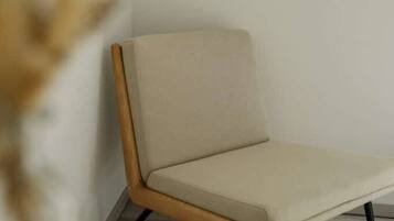 A modern chair with a wooden frame and a light-colored cushion, positioned against a plain wall.