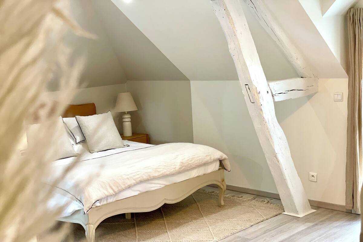 Ein Schlafzimmer mit Bett, Nachttisch, Lampe und Fenster.