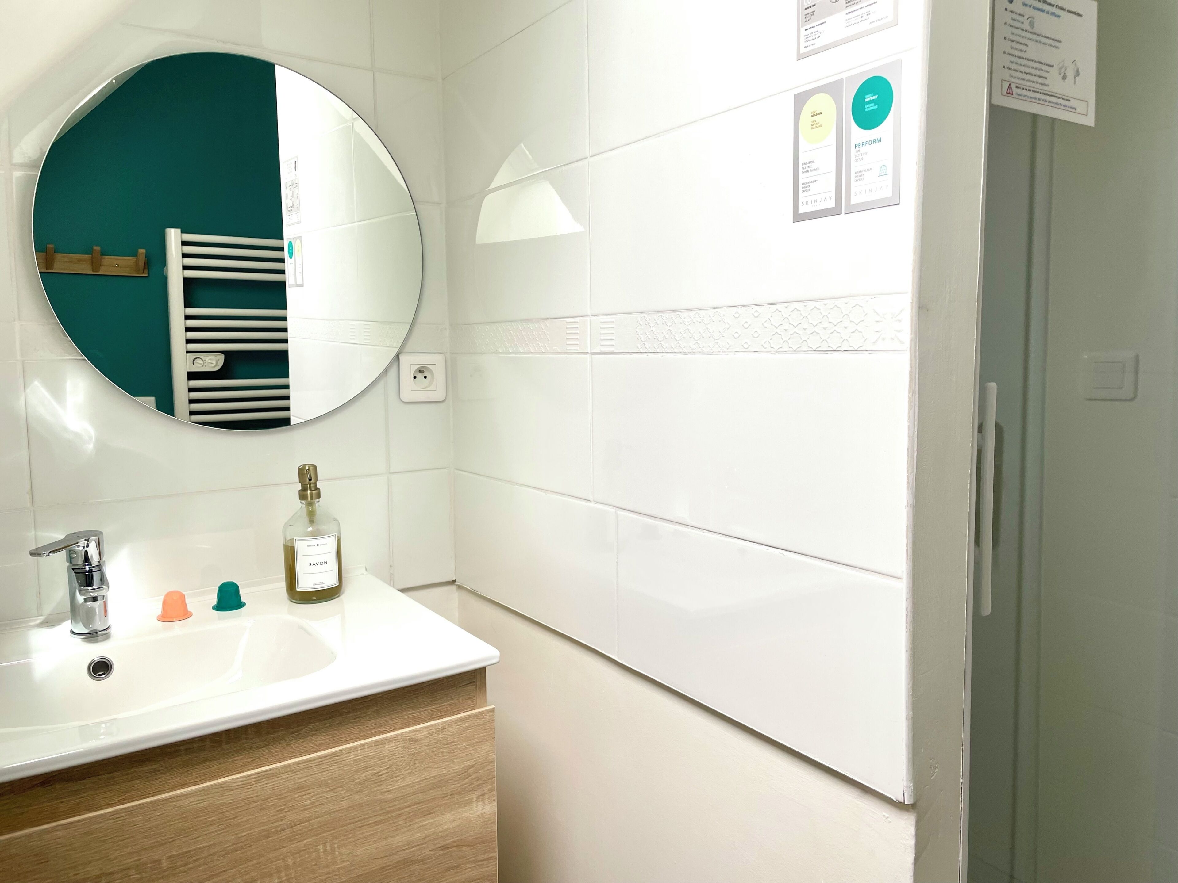 A bathroom with a white sink, a round mirror, a towel rack, and a bottle of soap.