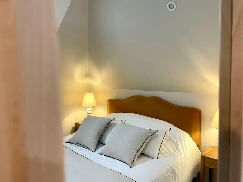 A neatly made bed with white bedding and two pillows, a wooden headboard, and a bedside lamp on a nightstand.