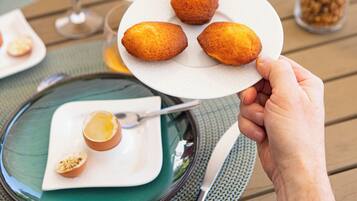 Una mesa de comedor con platos de comida, una mano sosteniendo un plato con croissants y un vaso de jugo de naranja.