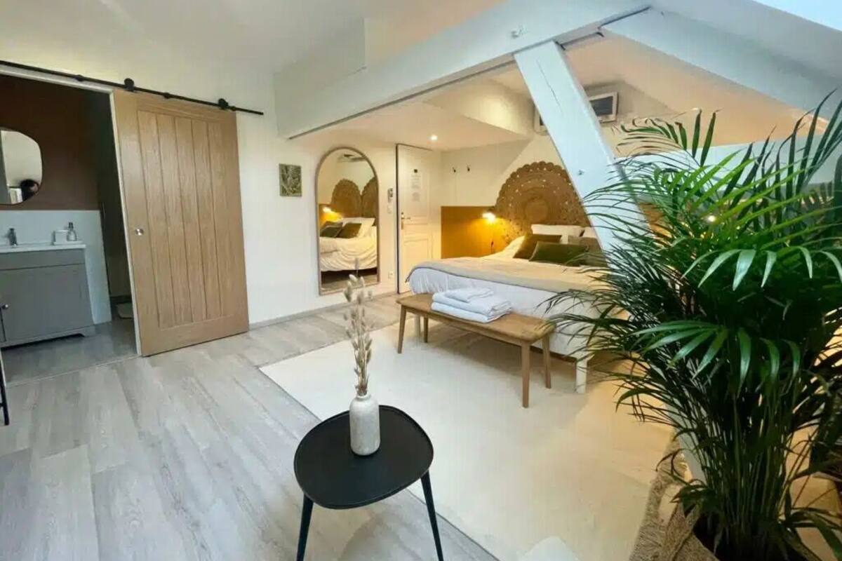 Ein Schlafzimmer mit einem Bett, einem Nachttisch und einem großen Spiegel. Eine Schiebetür führt ins Badezimmer.