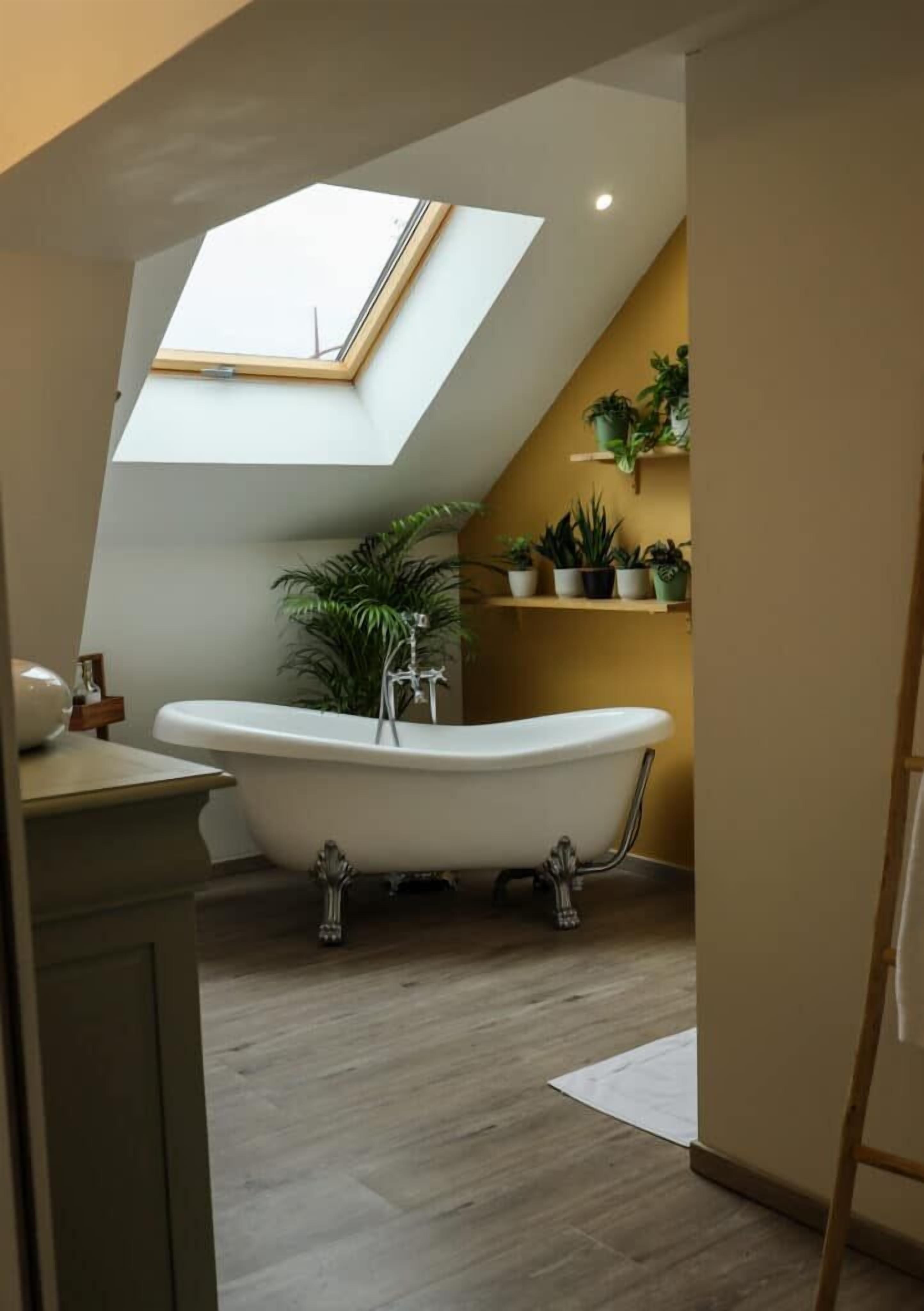 Ein modernes Badezimmer mit einer freistehenden Badewanne, einem Oberlicht und Blumentöpfen auf Regalen.
