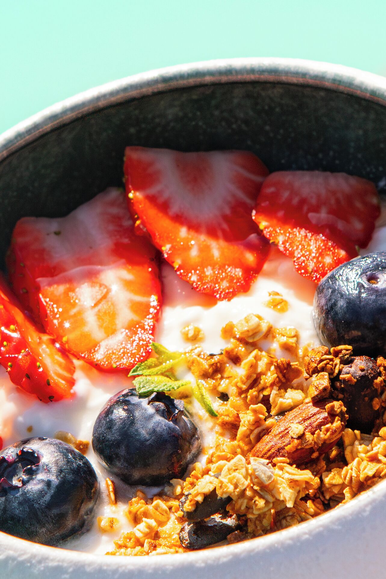 Un bol de yaourt garni de fraises, de myrtilles, de granola et d’une tranche de banane.