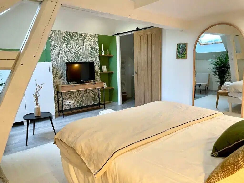 Un dormitorio con cama, televisor, armario y pared verde con diseño de hojas.