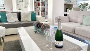 Een moderne woonkamer met een grijze bank, een witte bank en een salontafel met een fles champagne en twee glazen.