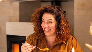 Iemand eet aan een tafel, met een bord eten, een glas wijn en een kaars.