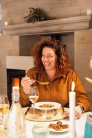 Una persona cenando en una mesa, con un plato de comida, una copa de vino y una vela.
